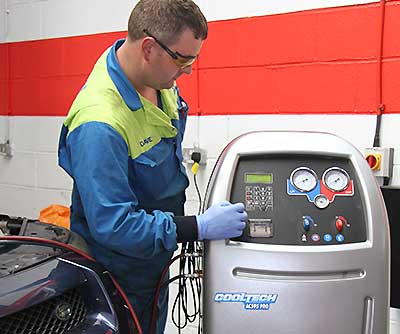 close up of a mechanic in blue overalls with excel automotives logo on his back performing a full high pressure air conditioning system clean on a volvo