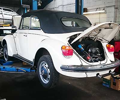 a volkswagon beetle in need of engine repairs with its boot lid up revealing a very poorly engine