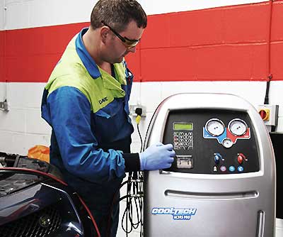 close up of a mechanic in blue overalls with excel automotives logo on his back performing a full high pressure air conditioning system clean on a volvo