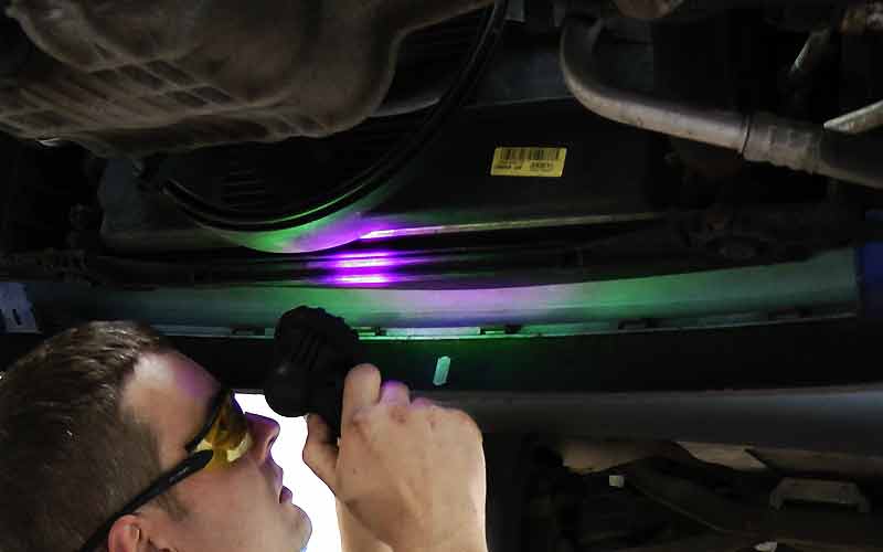 air conditioning specialist under a ford car using ultra violet light to source an air conditioning problem