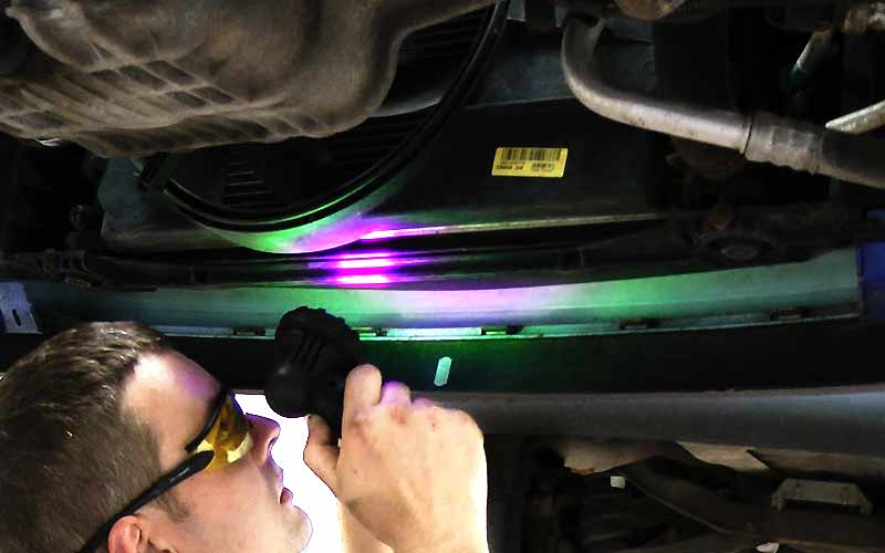 air conditioning specialist under a ford car using ultra violet light to source an air conditioning problem