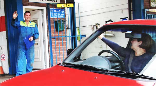 close up of excel automotives dave brown outside their chesterfield garage waving to a happy customer who is waving back as she leaves in her little red car