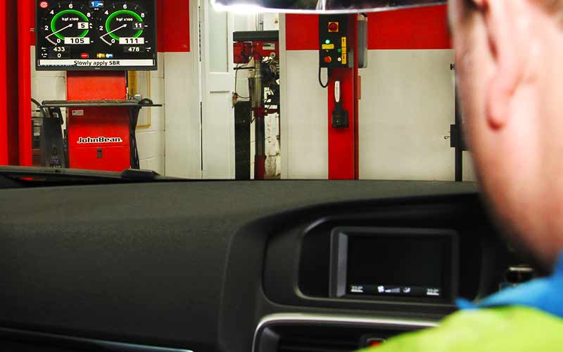 mot test screen showing 2 large dials indicating vehicle braking power seen through a car windscreen by an mot expert analysing and testing the vehicles brakes