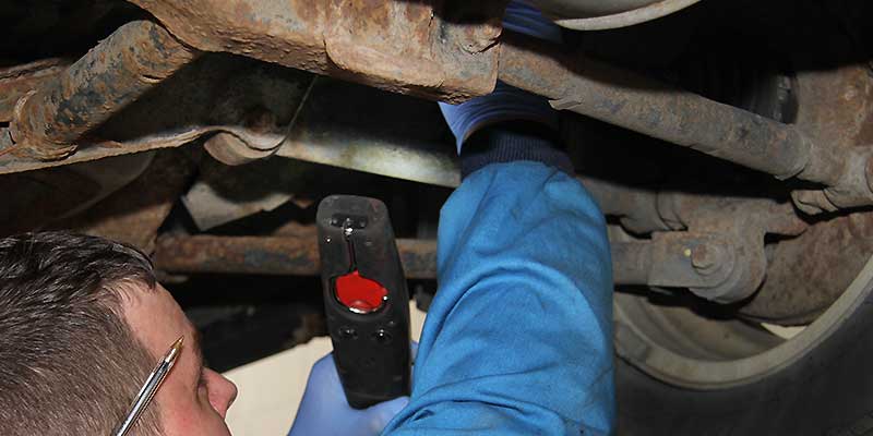 mechanic under a volvo up on a ramp shinning a very intense light around the vehicle exhaust, brakes and suspension